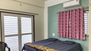 Una habitación con una cama, una silla, un ventanal con cortinas y un equipo de aire acondicionado.