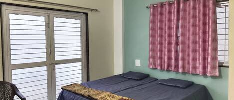 Een kamer met een bed, een stoel, een raam met gordijnen en een airconditioning.