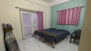 Una habitación pequeña y limpia con cama, una silla, cortina y puerta.