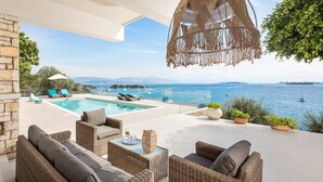 Un área junto a la piscina con mobiliario de mimbre, una lámpara colgante y vista al mar.