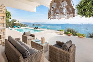 A poolside area with wicker furniture, a hanging light fixture, and a view of the sea. - Villa Anser - Four Bedroom Villa, Sleeps 10 (Limni)