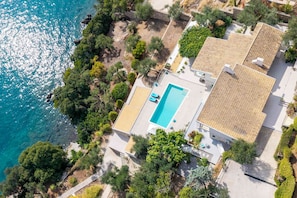 A residential property with a swimming pool, terraced roof, and surrounding vegetation.