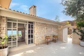 A stone building with a glass door entrance, outdoor seating area, and potted plants.