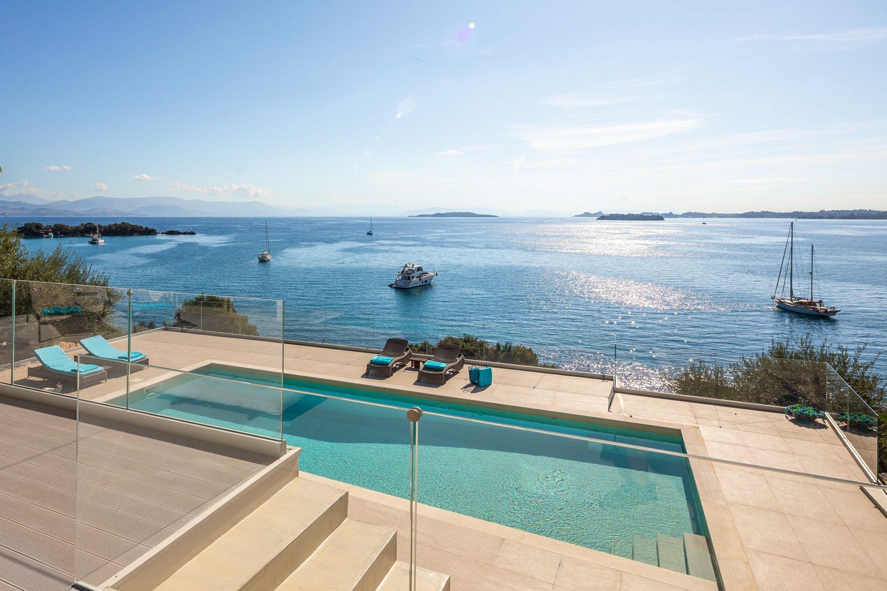 Ein Poolbereich mit klarem, blauem Wasser, Liegestühlen und Blick auf Boote auf dem Wasser.