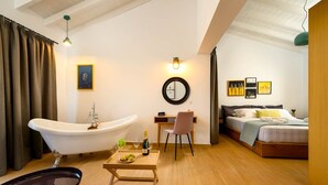 Ein modernes Schlafzimmer mit einer großen Badewanne, einem Schreibtisch mit Stuhl, einem Bett und einem kleinen Tisch mit Flasche und Gläsern.