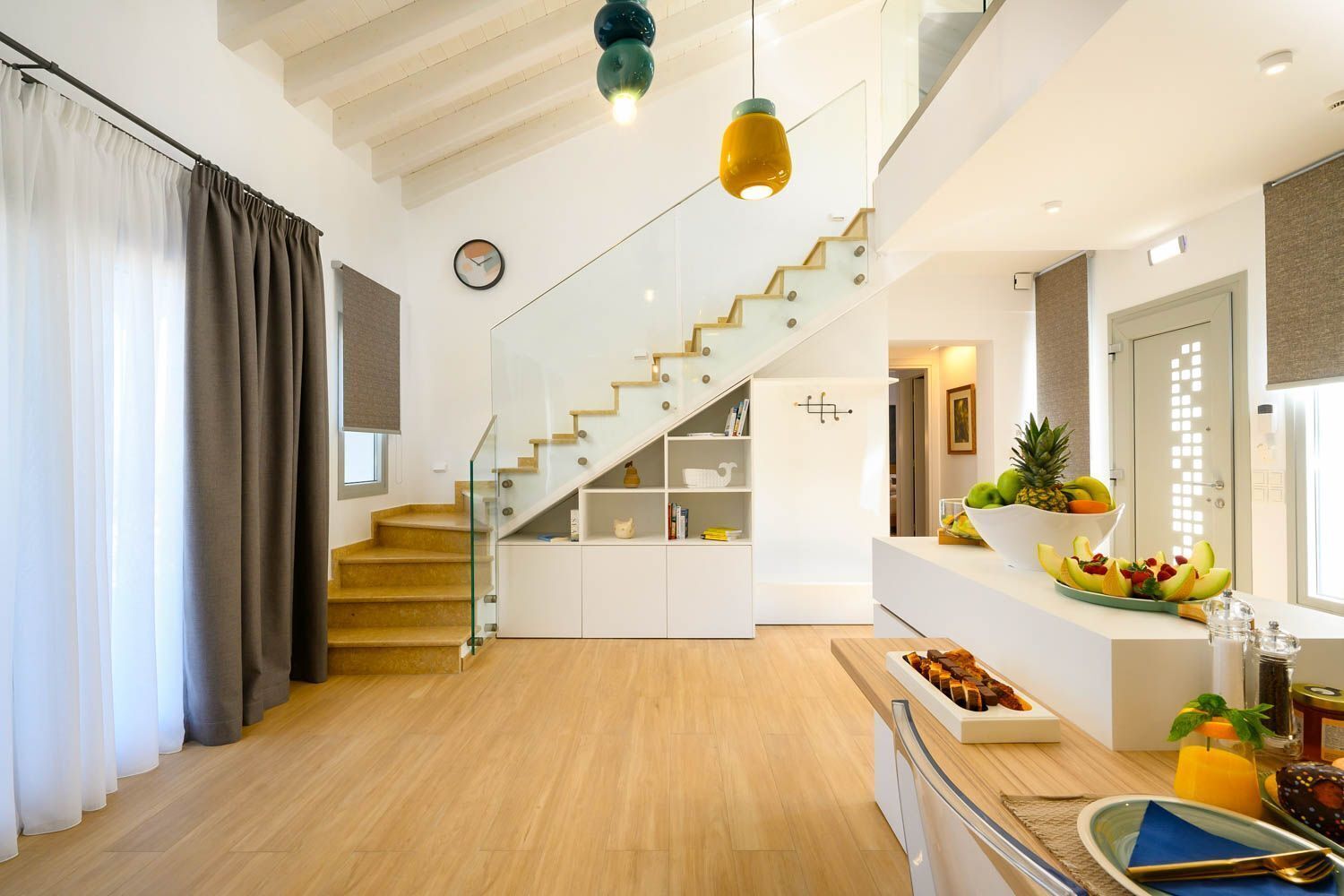 A modern interior with a staircase, wooden flooring, and a kitchen area with fruit and snacks.