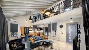A spacious living area with a modern sofa, a black armchair, and a coffee table. There is a kitchen in the background with a dining table and chairs.