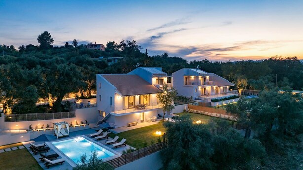A modern two-story house with a swimming pool, outdoor seating, and a well-lit patio area.