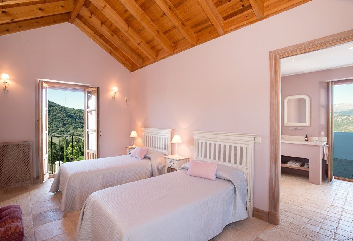 A bedroom with two beds, a balcony with a view, and a bathroom with a mirror.