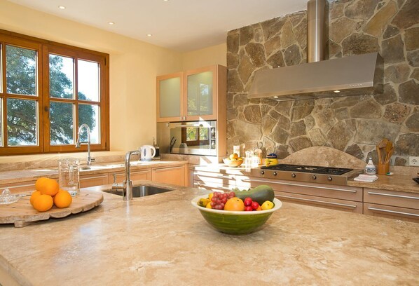 Una cocina moderna con salpicadero de piedra, un ventanal y un frutero en la encimera.