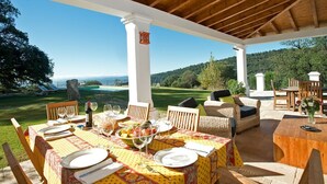 An outdoor dining area with a table set for four, surrounded by wicker furniture, under a wooden pergola with a view of a golf course and hills. - Villa Gaucin - Six Bedroom Villa, Sleeps 12 (El Colmenar)