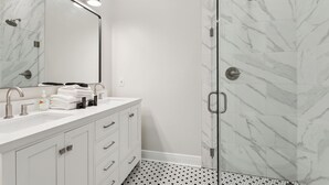A modern bathroom with a marble shower wall, a white vanity with a mirror and lights, and a tiled floor.