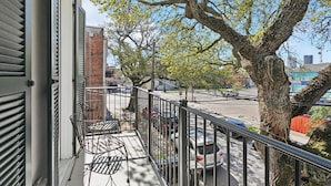 A balcony with a metal railing, a metal chair, and a tree with green leaves.