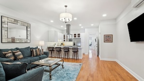 A modern living room with a sofa, coffee table, and a dining area with bar stools.