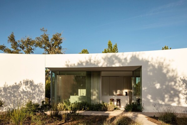 Une maison moderne dotée d’une grande baie vitrée, d’un petit espace extérieur aménagé pour s’asseoir et d’un chemin menant à l’entrée.