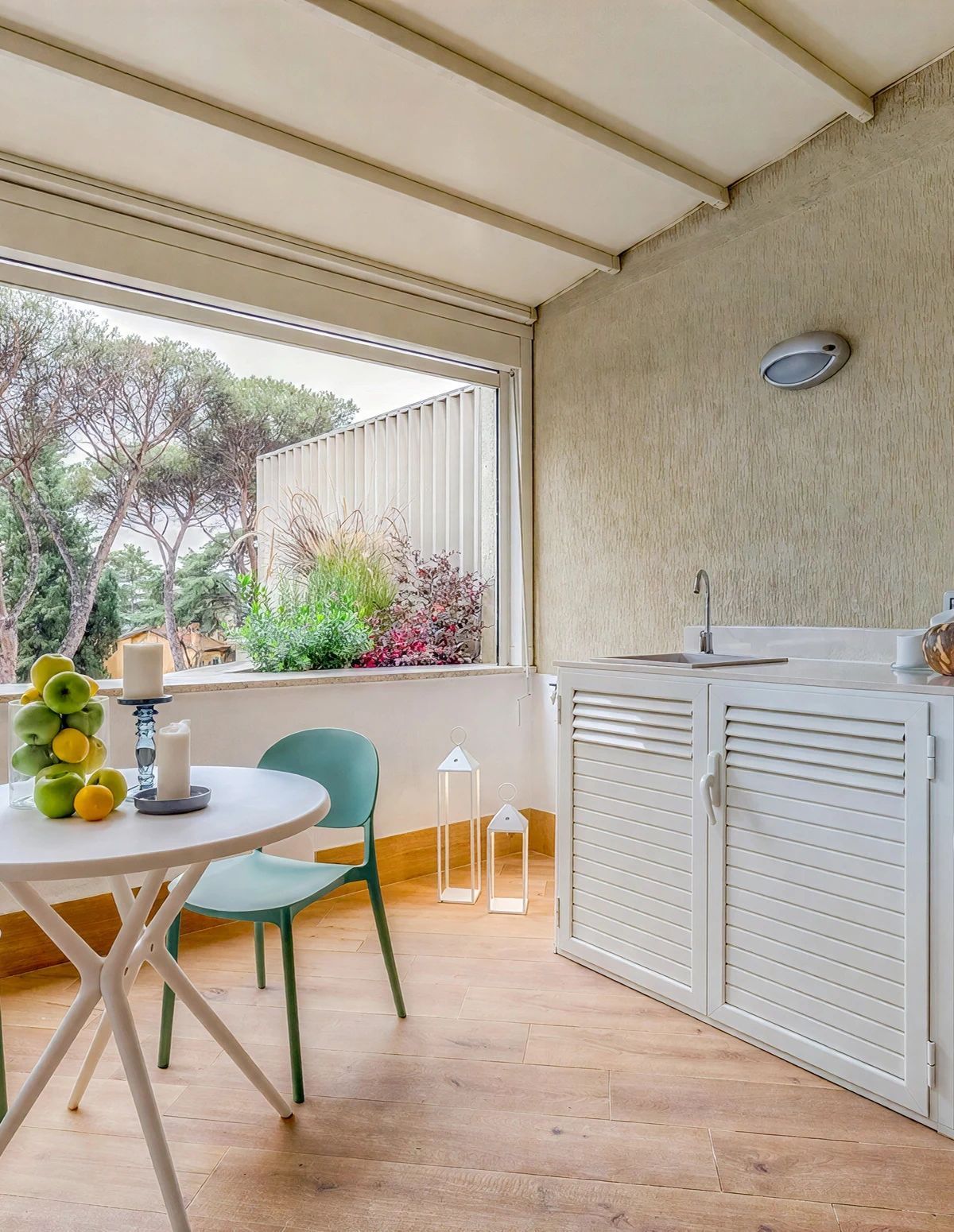 Un espace patio comprenant une table ronde, des chaises, un meuble blanc et une fenêtre donnant sur un espace verdoyant.