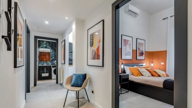 A modern hotel room with a bed, bedside table, and a chair. There is a hallway leading to a bathroom with a mirror and sink. - Apartment Apriale - Two Bedroom Villa, Sleeps 5 (Rome)