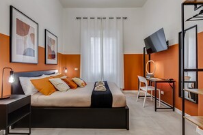 Quarto de hotel moderno com cama, escrivaninha com cadeira, televisão na parede e obras de arte nas paredes.