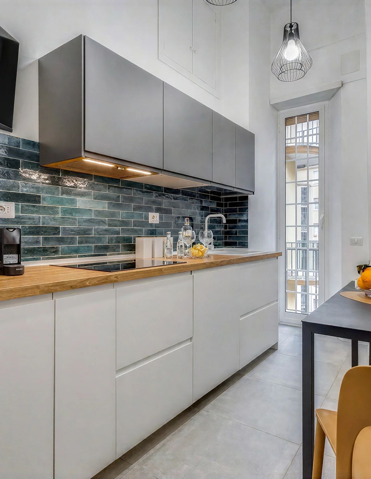 A modern kitchen with a wooden countertop, white cabinets, and a backsplash of dark tiles.
