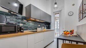 A modern kitchen with a microwave, coffee maker, and a wooden countertop. There is a dining table with a chair and a fruit bowl. - Apartment Apriale - Two Bedroom Villa, Sleeps 5 (Rome)