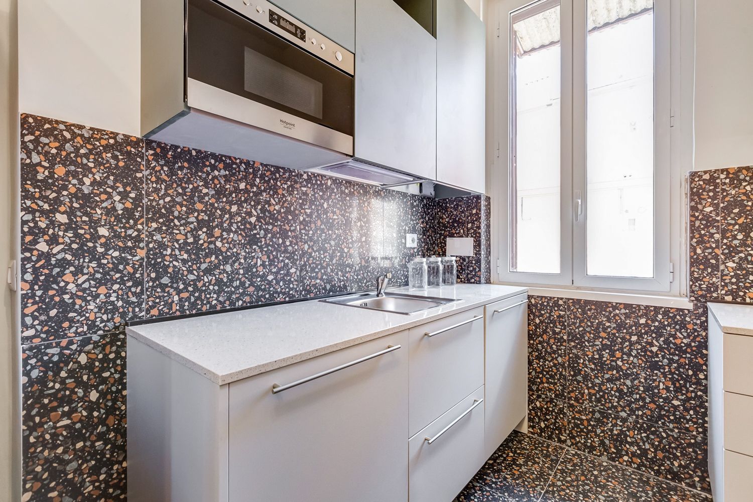 Una cucina con mobili bianchi, forno integrato e una finestra.