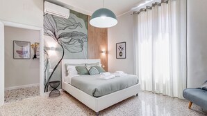 A modern bedroom with a white bed, a large abstract wall art, a wooden panel wall, and a grey sofa. - Velcro Apartment - Three Bedroom Villa, Sleeps 7 (Rome)