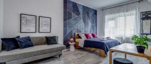 Ein modernes Schlafzimmer mit Sofa, Bett mit blau-weißer Bettdecke, einem kleinen Tisch und einer Topfpflanze.