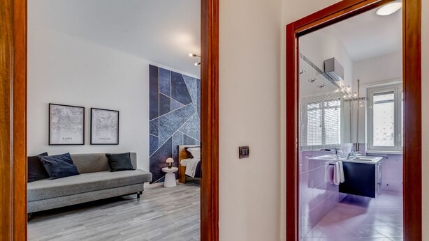 Een moderne woonkamer met een grijze bank, een klein bijzettafeltje en een muur met abstracte kunst.