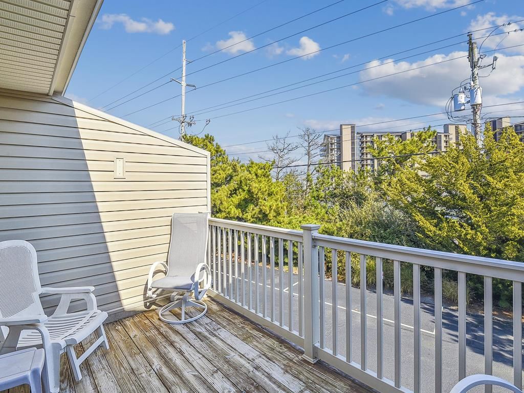 A wooden deck with two white chairs, a white railing, and a view of a road and buildings in the background.