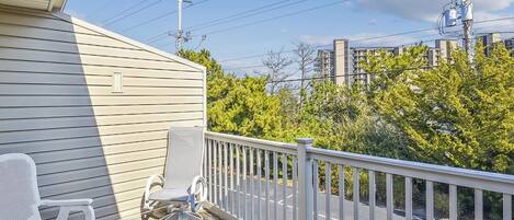 A wooden deck with two white chairs, a white railing, and a view of a road and buildings in the background.
