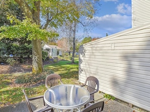 A patio with a round table and chairs, a tree, and a house with white siding.