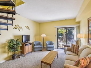 A living room with a sofa, two armchairs, a coffee table, a TV, and a staircase.