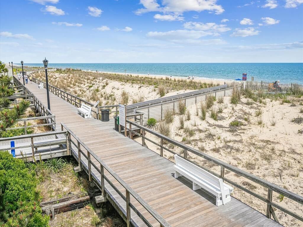 A wooden boardwalk leading to a beach with sand dunes and a clear blue sky.