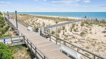 A wooden boardwalk leading to a beach with sand dunes and a clear blue sky.
