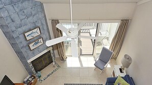 A living room with a fireplace, ceiling fan, and a view of the balcony.