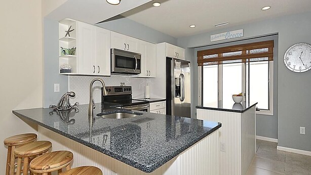 A modern kitchen with white cabinetry, a granite countertop, and a built-in microwave.