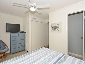 A bedroom with a bed, a dresser, a ceiling fan, a door, and a wall-mounted artwork. - Stylish 4BR by Bethany Beach Boardwalk | Sleeps 10 (Bethany Beach)