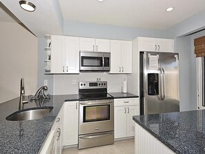 A modern kitchen with white cabinets, stainless steel appliances, granite countertops, and a built-in oven.