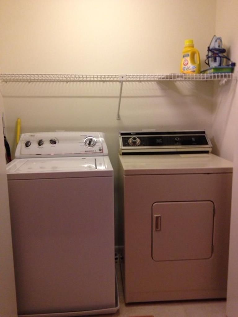 Un cuarto de lavandería con dos lavadoras y un estante con productos de limpieza.
