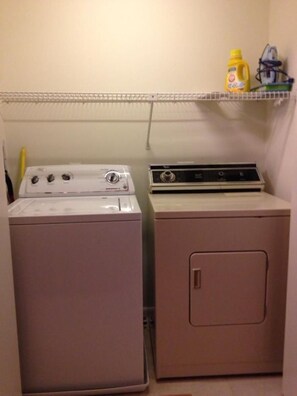 A laundry room with two washing machines and a shelf with cleaning supplies.