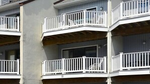 A multi-story building with balconies, a car parked in a garage, and a clear sky.