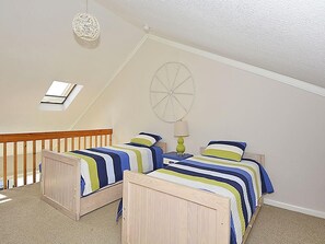A bedroom with two wooden beds, a ceiling fan, a wall clock, and a small window.