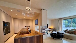 A modern kitchen with a central island, built-in appliances, and a dining area with a sofa and table. - Eclat de Provence - luxury villa - calanques de cassis - (Allauch)