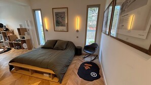 A modern bedroom with a wooden floor, a bed with a wooden frame, a rocking chair, and a black rug with a logo. - Eclat de Provence - luxury villa - calanques de cassis - (Allauch)