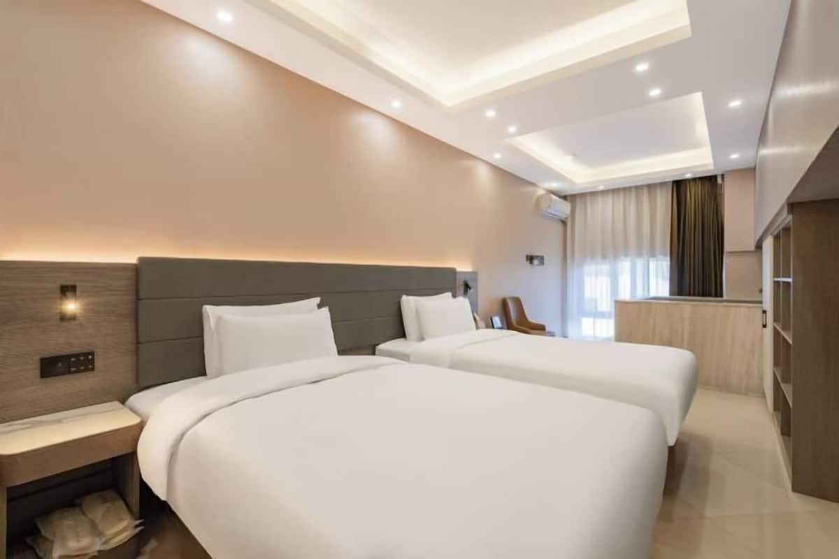 Quarto de hotel moderno com duas camas, uma mesa de cabeceira, escrivaninha e armário embutido.