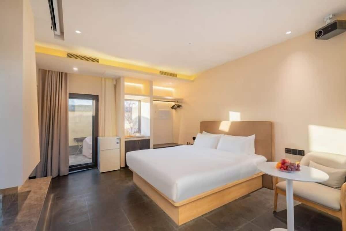 Quarto de hotel moderno com uma cama grande, mesa de cabeceira e uma pequena mesa redonda com frutas.