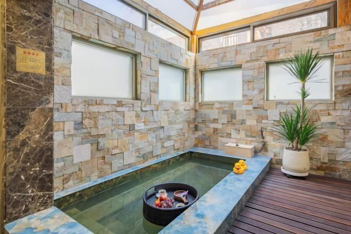 Uma área de spa com parede de pedra, uma pequena banheira de hidromassagem e um deck de madeira.
