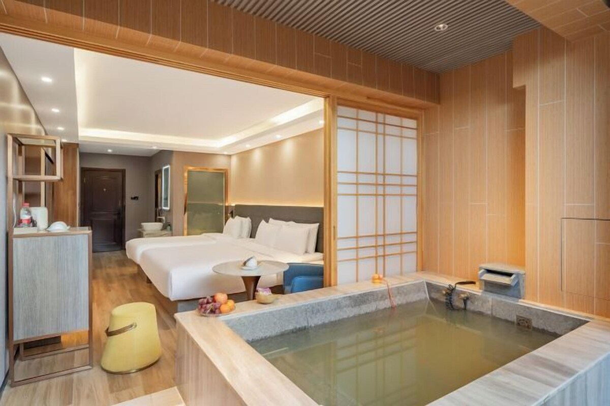 A hotel room with a bed, a small table, a bathtub, and a wooden partition.