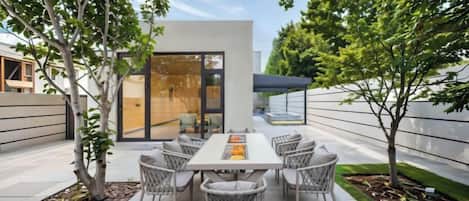 Terrassa exterior amb taula i cadires, envoltada d'arbres i un edifici modern.
