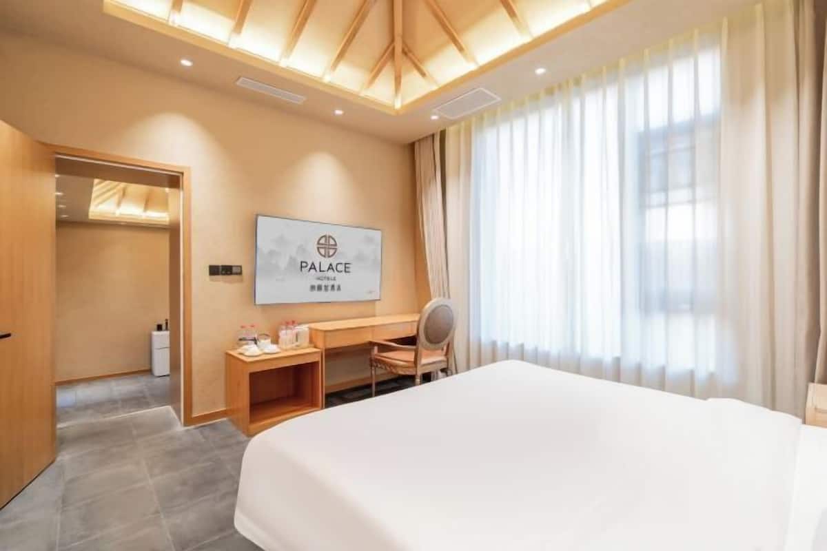 Quarto de hotel com cama, escrivaninha, cadeira, espelho e janela com cortinas.